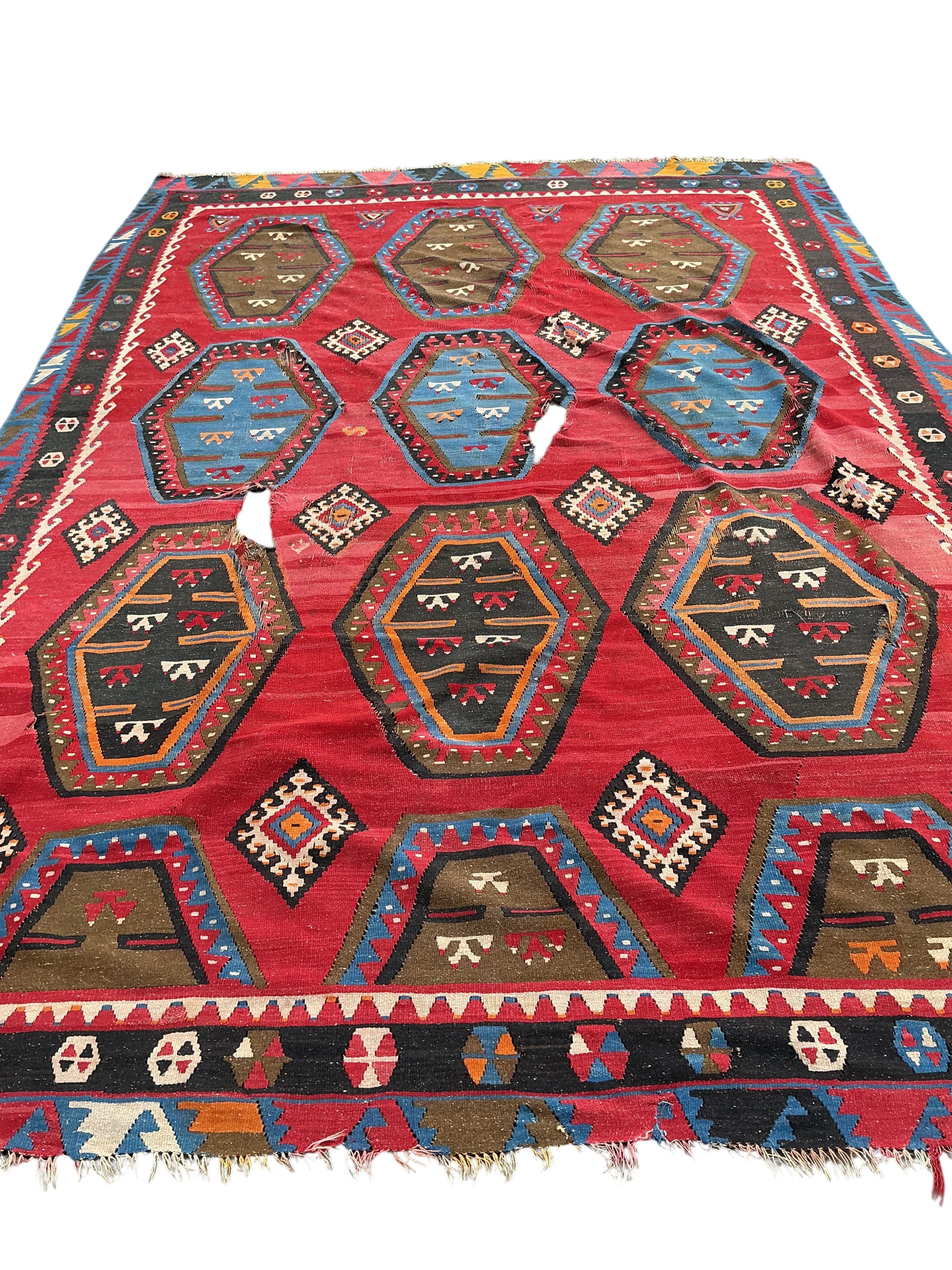 A Turkish Kilim flatweave polychrome carpet, woven with three rows of hexagons, on a red ground, (severely holed and damaged in places), 373 x 267cm
